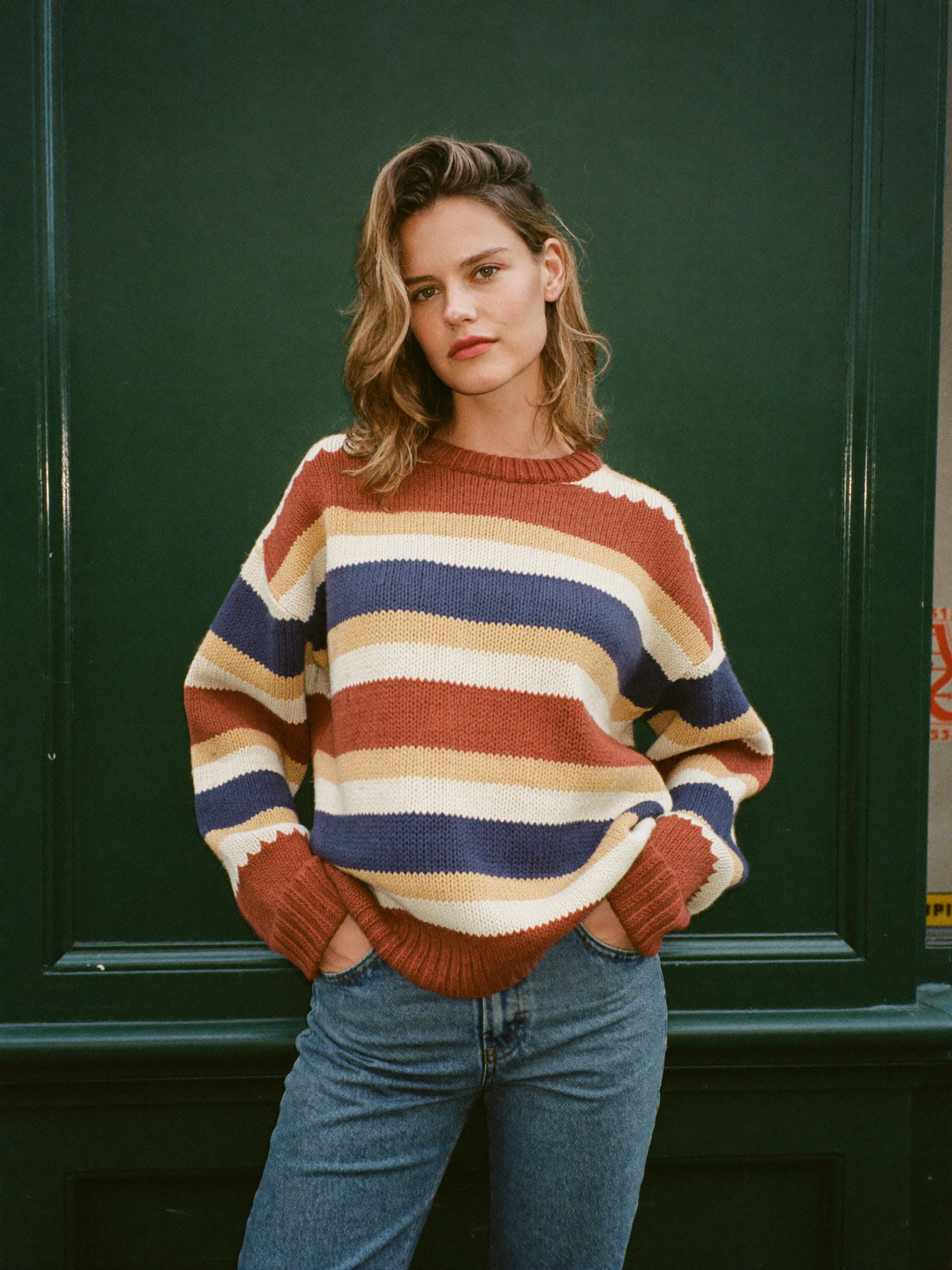 A woman in a bold multi-colour striped knit sweater against a deep green shopfront