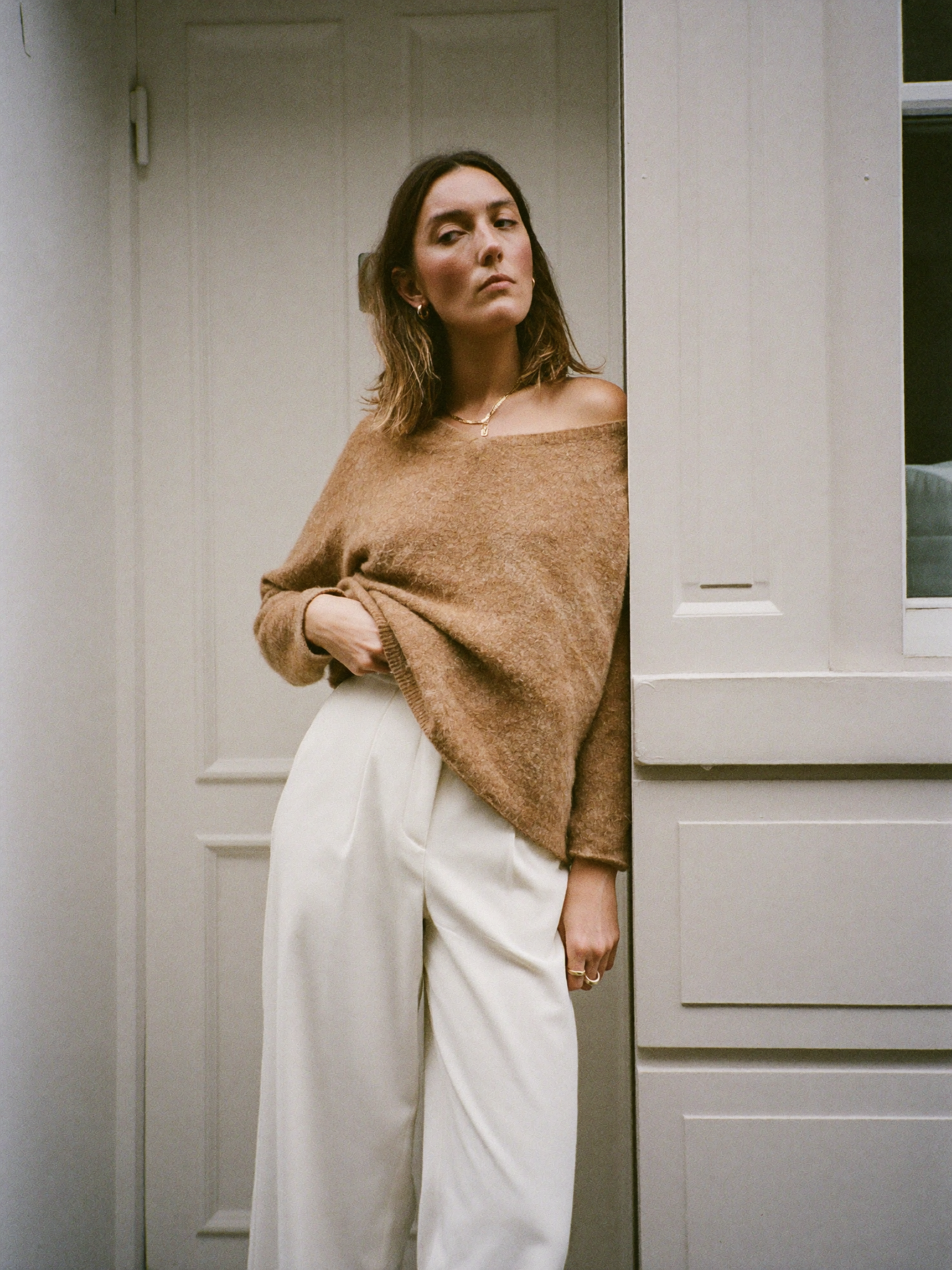A woman in a camel knit sweater and ivory wide trousers in a townhouse doorway