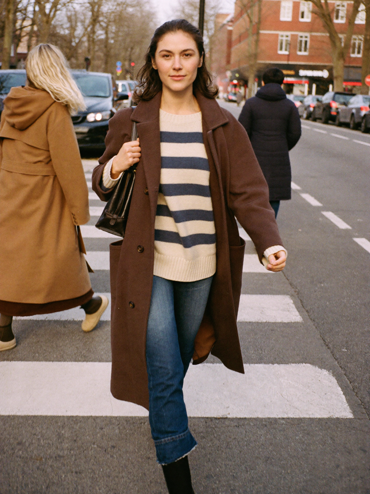 Lookbook - a woman crossing a city street in a striped knit sweater under an open espresso brown wool coat